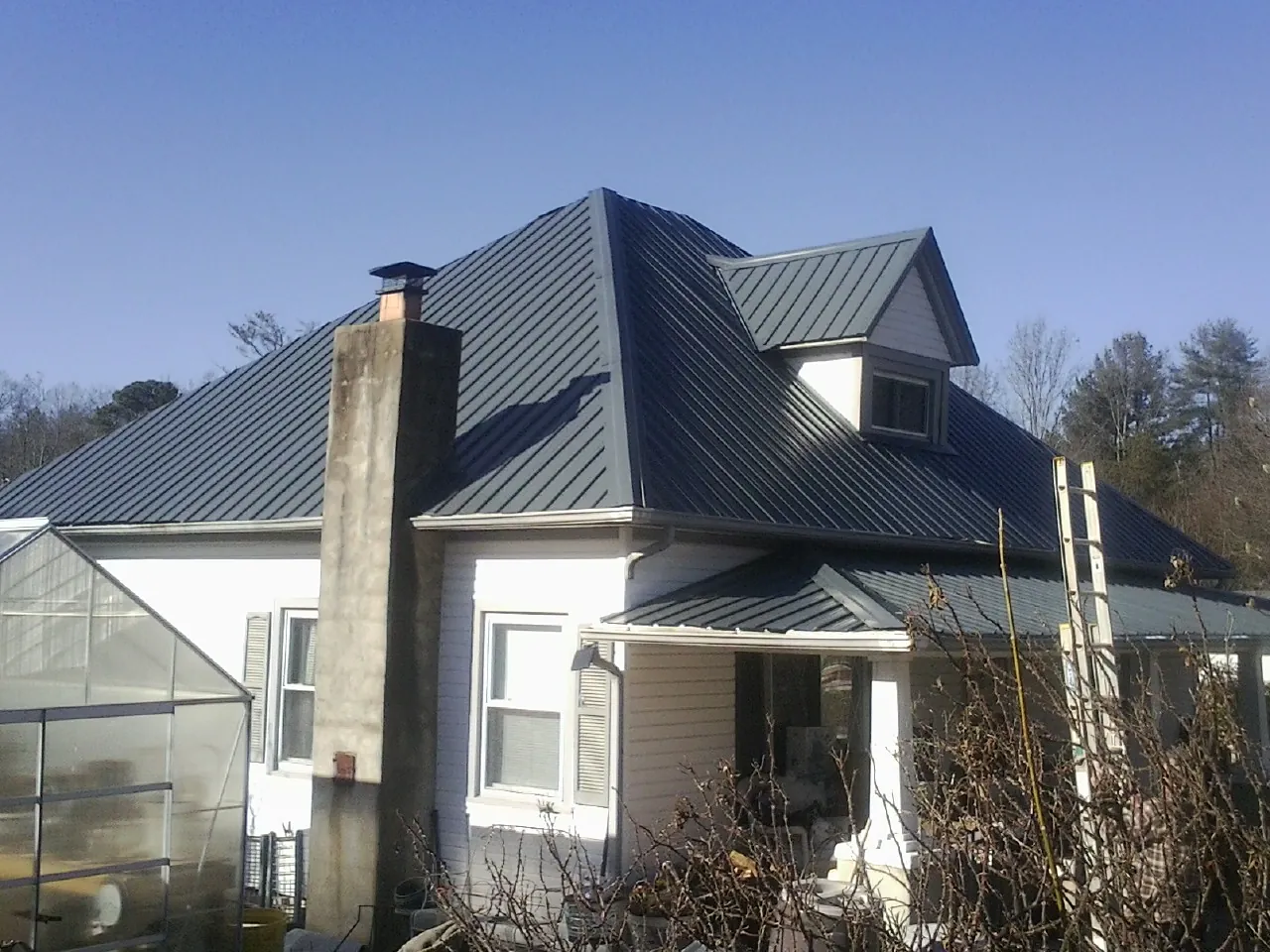 Dark blue standing seam metal roof on a white farmhouse with dormer — Slate & Tile Roof Repair by Roofing Brothers in Fort Laramie