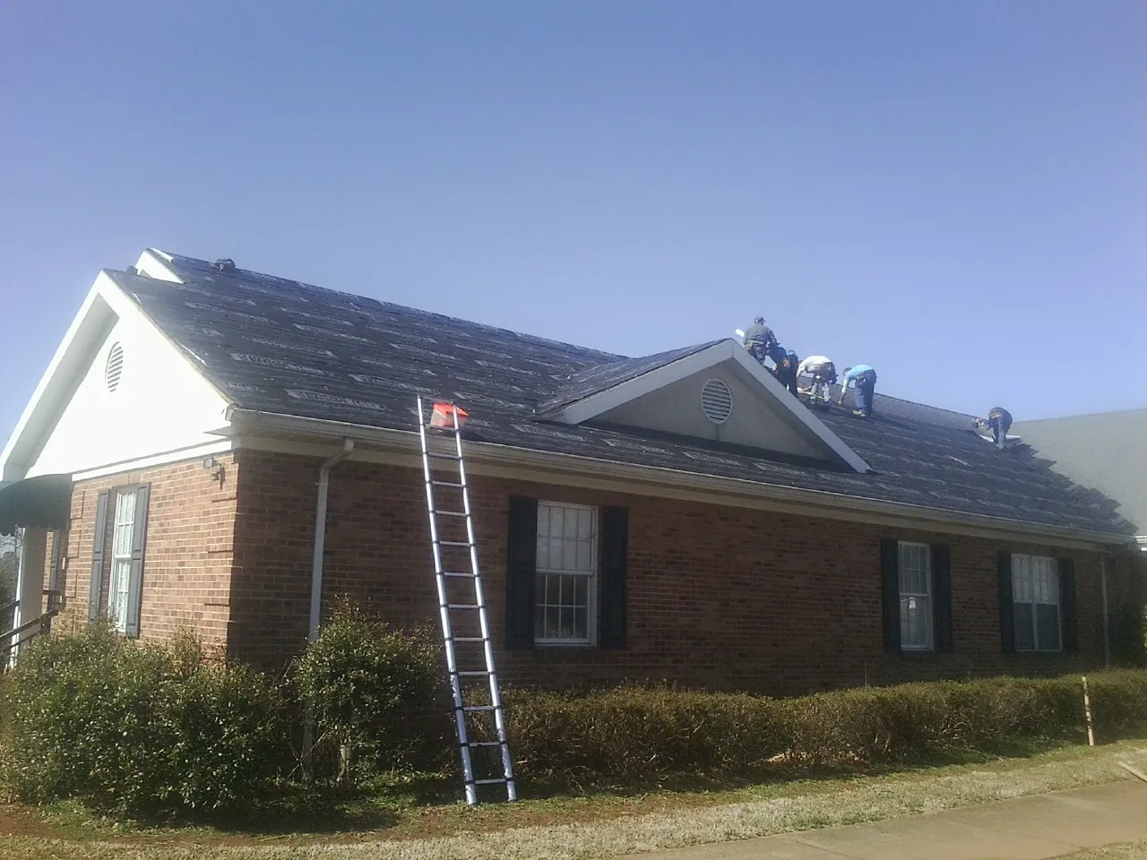 Crew tearing shingles off a brick ranch roof with a ladder set — Emergency Roof Repair work by our crew in Fort Laramie