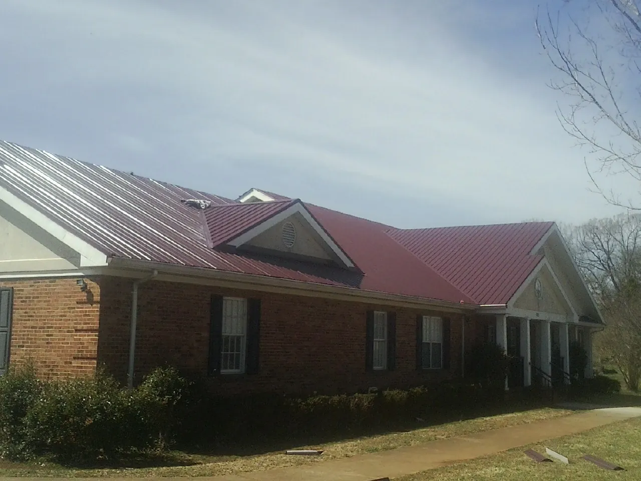 Red metal roof with gabled entries on a long brick building, from a Hail Damage Roof Repair job in Fort Laramie
