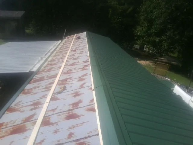 Old rusted panels beside newly installed green metal roofing — Wind Damage Roof Repair by Roofing Brothers in Fort Laramie