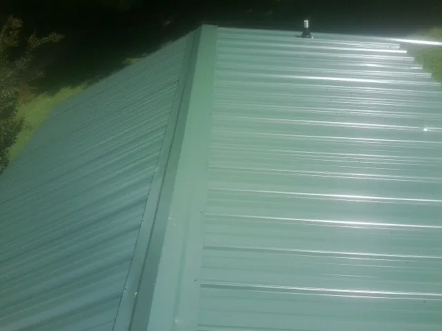New green metal panels meeting at the ridge of a roof — Flat Roof Repair work by our crew in Fort Laramie
