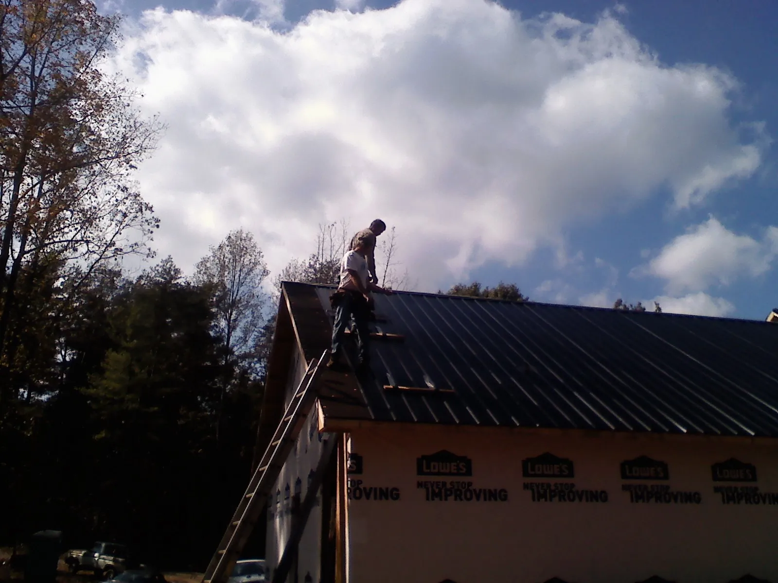 Roofer fastening dark metal panels high against a cloudy sky, from a Roof Inspection job in Fort Laramie