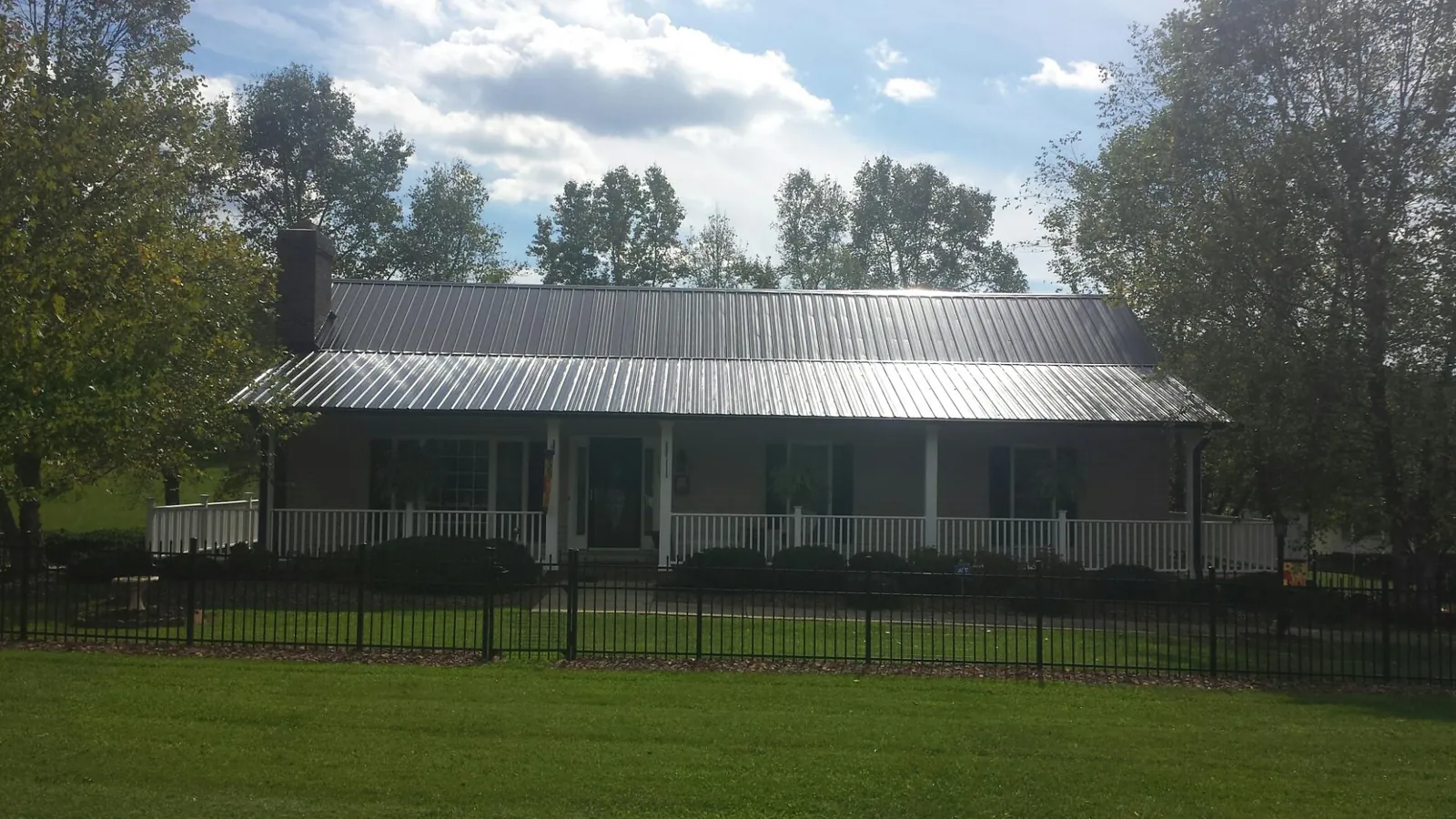 Gray metal roof on a brick ranch with a full width front porch — Gutter Guard Installation work by our crew in Fort Laramie