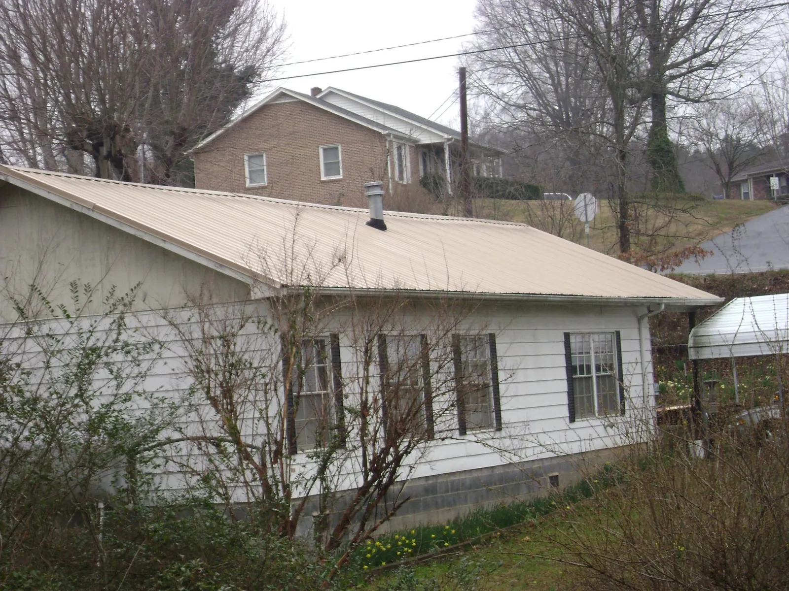 Tan metal roof on a white sided house set into a hillside — Commercial Roofing by Roofing Brothers in Fort Laramie