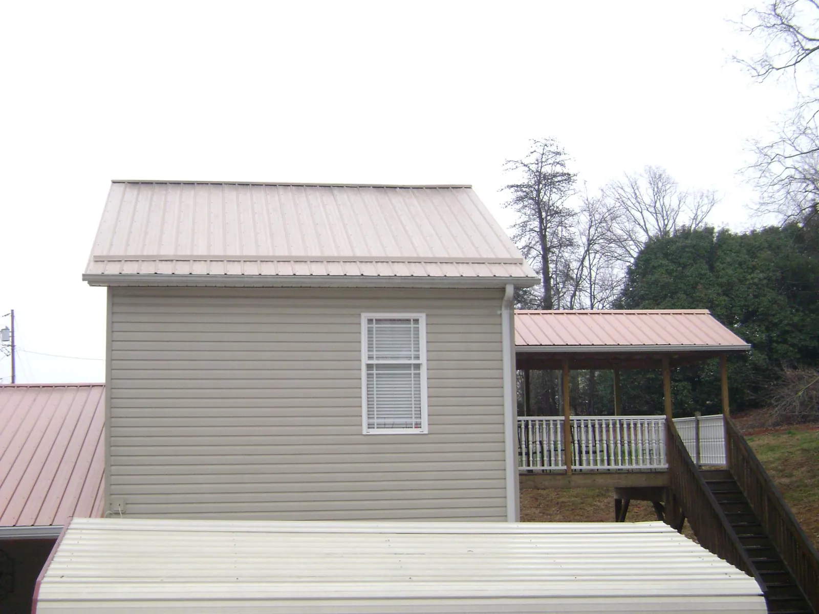 Tan metal roofs on a two story addition and attached porch, from a Roof Replacement job in Fort Laramie